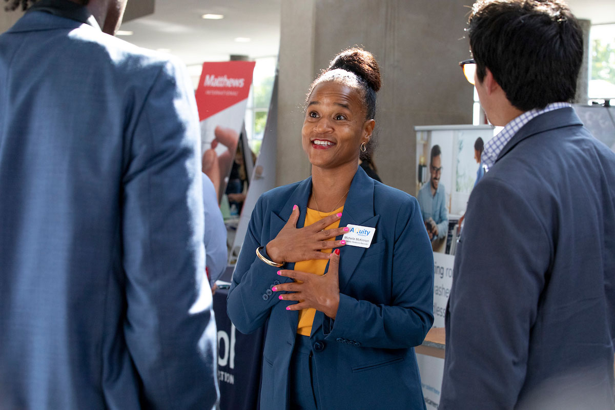 A woman in a business suit smiling and speaking with a group of students