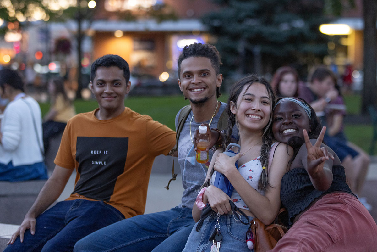 Four students smiling and posing on campus for an evening photo